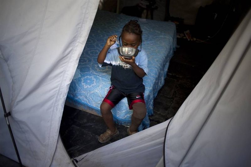 Вот Шнэйли Симильен завтракает в потрепанной палатке. Эта палатка в городке Леоган теперь служит домом для всей его семьи из пяти человек. В начале ноября, когда над Гаити пронесся ураган Томас, палатка была еще больше повреждена. Протез левой ноги, который мальчик получил в марте, уже начинает понемногу ломаться, но у семьи нет средств, чтобы обратиться за помощью в госпиталь Альберта Швейцера, который находится в городе Дешапель.