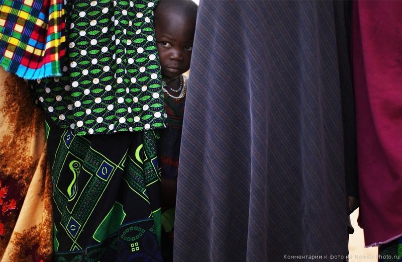 29. Четырёхлетний Норто Юсеф Мухаммед выгладывает из-за стоящих женщин, пока его мама интересуется подробностями переселения в другой лагерь. 24 августа 2008 года, Дадааб, Кения.