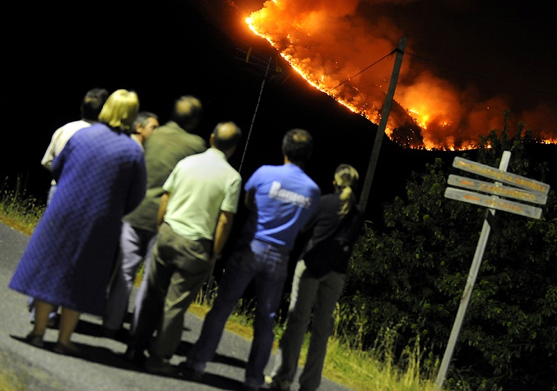 Жители наблюдают за лесным пожаром недалеко от испанского города Авила. Власти сообщают, что водитель бульдозера, участвующий в борьбе с огнем, и еще один человек погибли во время пожара во вторник. (Pierrephilippe Marcou/AFP/Getty Images)