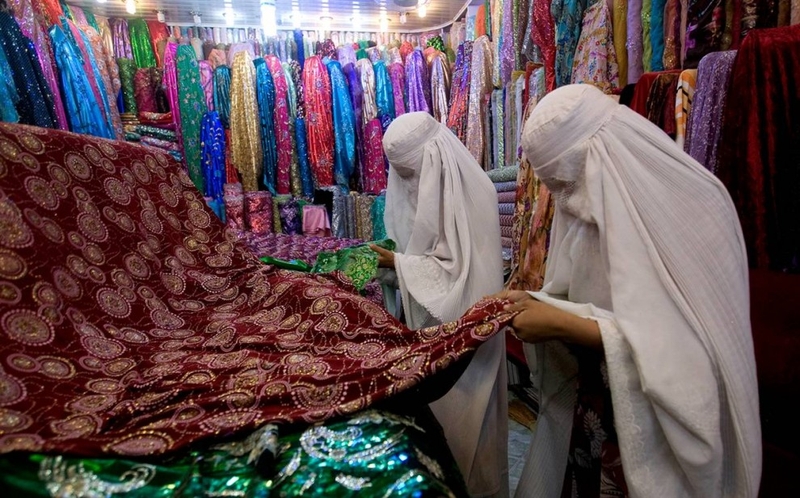 Одетые в паранджу афганские женщины выбирают ткани в магазине в Мазари-Шарифе 3 сентября.
