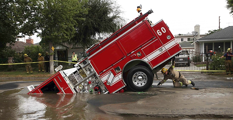 Пожарный из Лос-Анджелеса заглядывает под пожарную машину, которая застряла в водосточном колодце в районе Лос-Анджелеса Веллей Вилладж. Четверо пожарных чудом избежали травм после того, как 22-тонная пожарная машина ушла в большую яму, причиной образования которой стала авария водопровода.