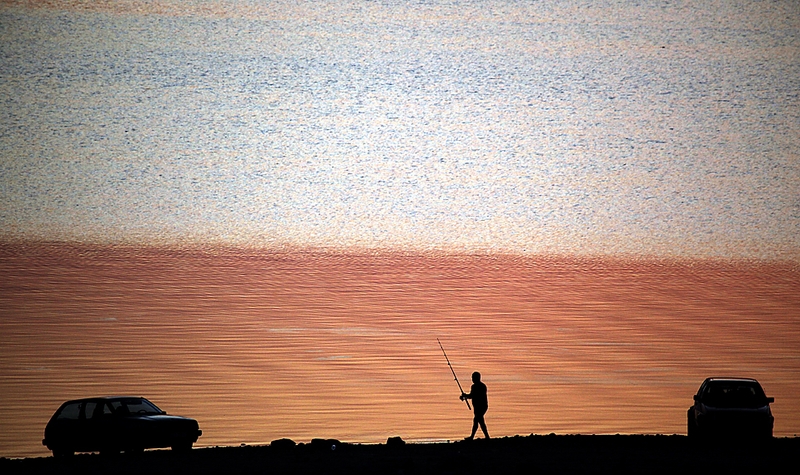 Рыбак идет вдоль озера на закате возле деревни Chenge в Болгарии. 