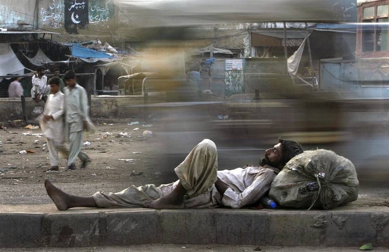 Автомобили проезжают мимо собирателя макулатуры, который спит на улице рано утром 13 сентября в пакистанском городе Карачи.