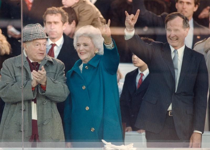 Президент Джорж Буш (старший) и миссис Барбара Буш  Президент Джорж Буш (старший) и Миссис Барбара Буш вместе с Бобом Хоупом на президентской трибуне во время инаугурационного парада 20 января 1989. Хоуп был его главнокомандующим. (Члены семьи Бушей, на заднем плане, включая Джорджа Буша младшего). Горизонтальные полосы на фото из-за отражений в стекле президентской трибуны. 