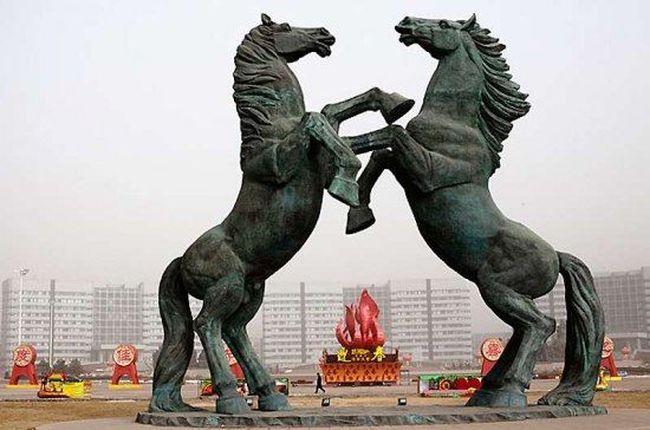 Памятник. Пешеход идет по улице позади гигантской скульптуры изображающей двух лошадей на площади Линьюйнли, район Кангбаши.