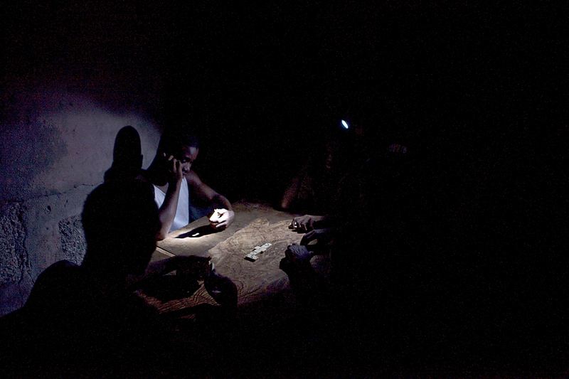 Люди играют в домино в свете фонарика в Порт-о-Пренс, Гаити. В большинстве городов в Гаити электричество дают только на несколько часов в день из-за недостаточного производства электроэнергии.